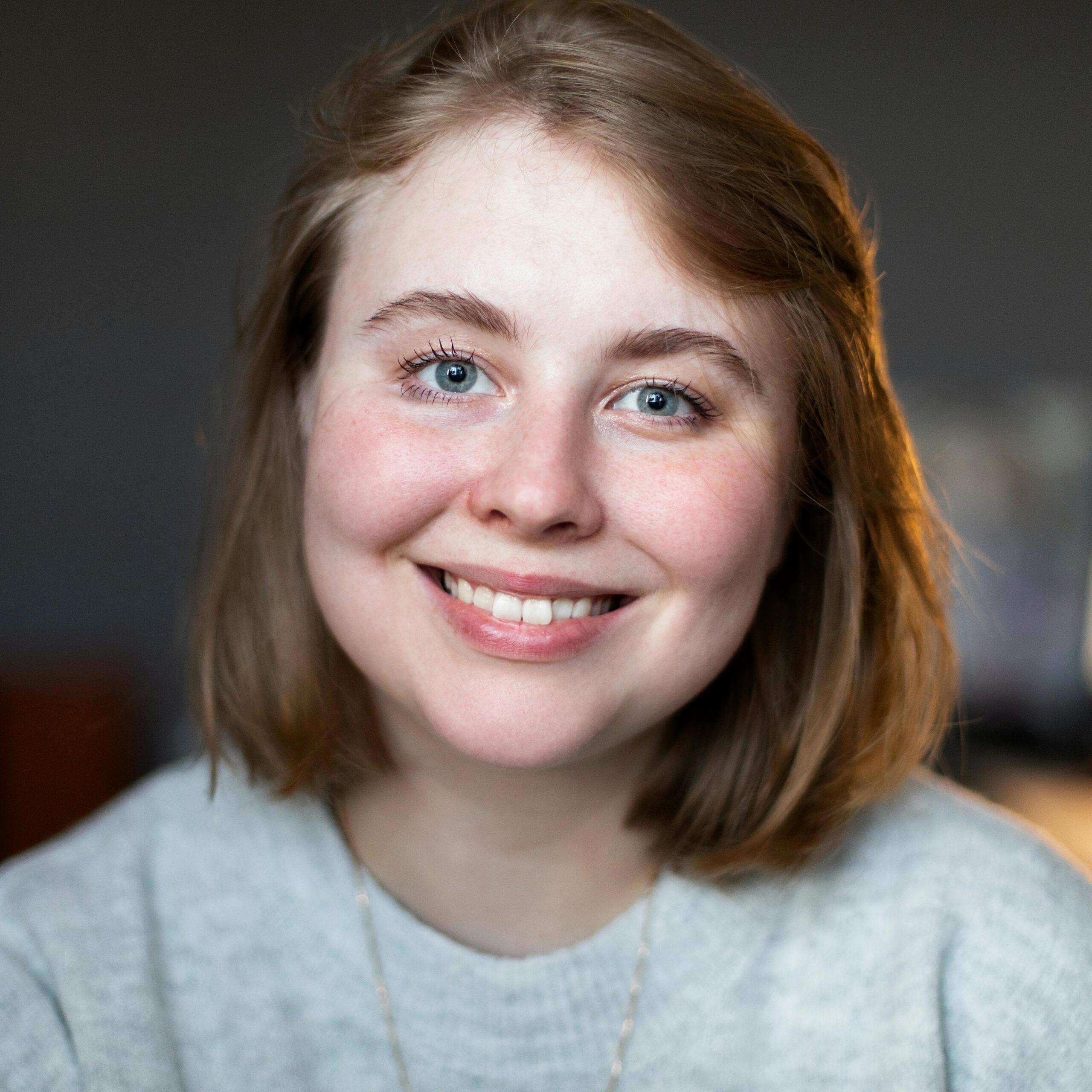 A cheerful woman with short blonde hair smiling indoors, showcasing natural beauty.
